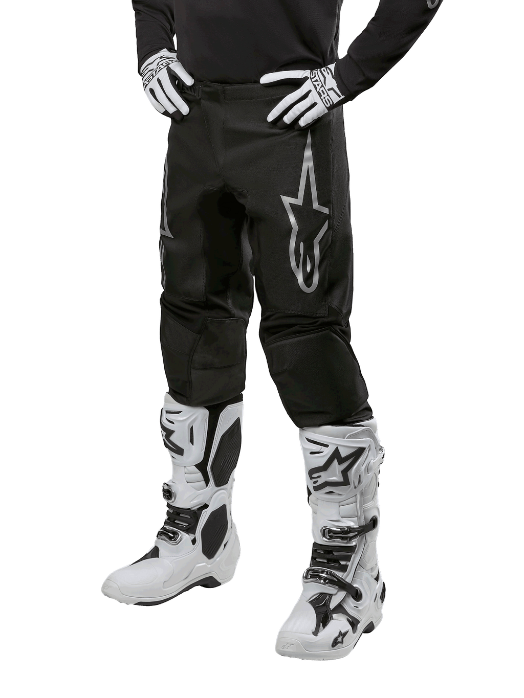 Spodnie Alpinestars 2024 Fluid Graphite, spodnie motocrossowe, szare i czarne, noszone z biało-czarnymi butami i rękawicami motocrossowymi, z dużym srebrnym logo Alpinestars na udzie, sportowy krój do jazdy terenowej
