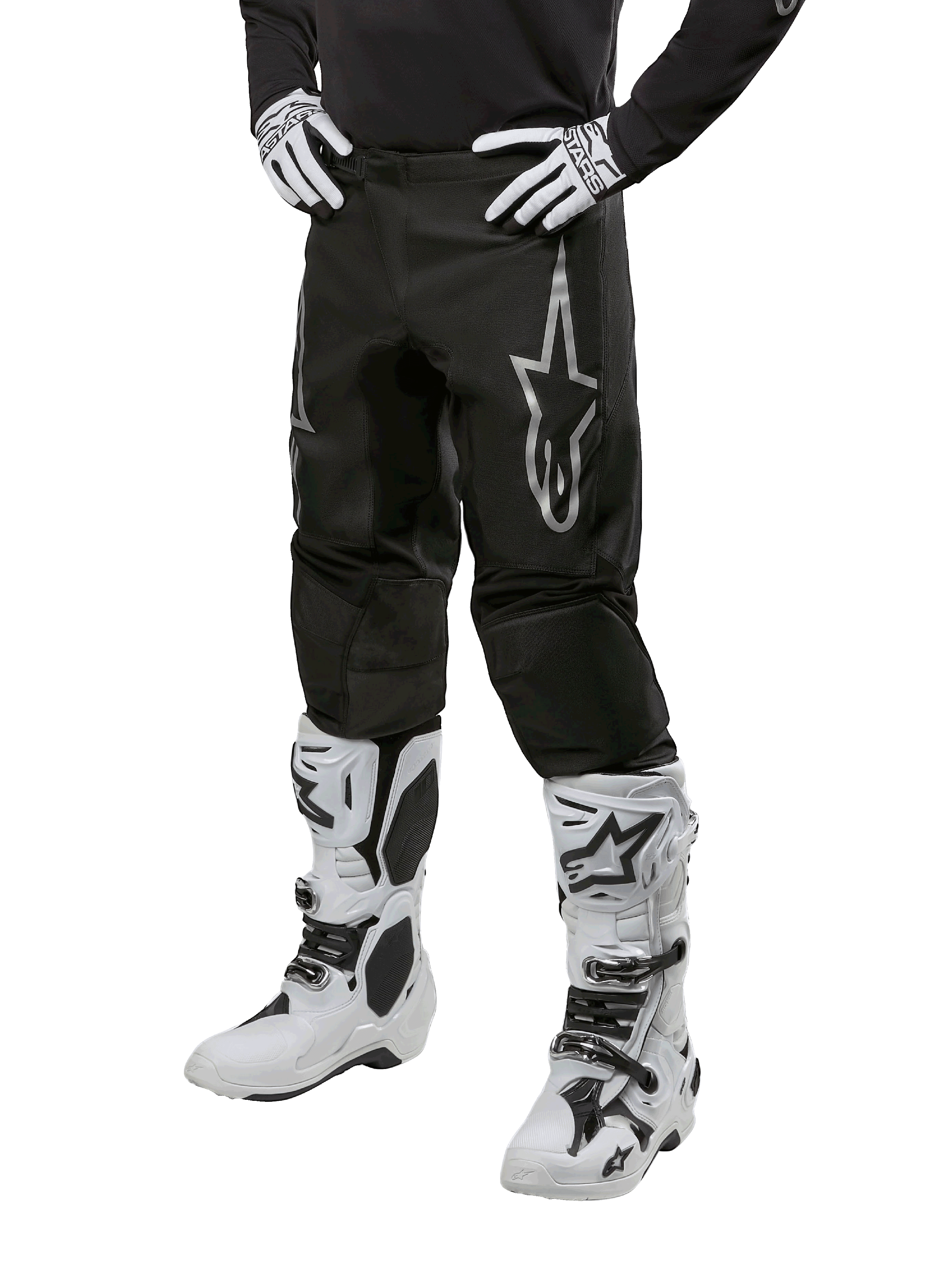 Spodnie Alpinestars 2024 Fluid Graphite, spodnie motocrossowe, szare i czarne, noszone z biało-czarnymi butami i rękawicami motocrossowymi, z dużym srebrnym logo Alpinestars na udzie, sportowy krój do jazdy terenowej