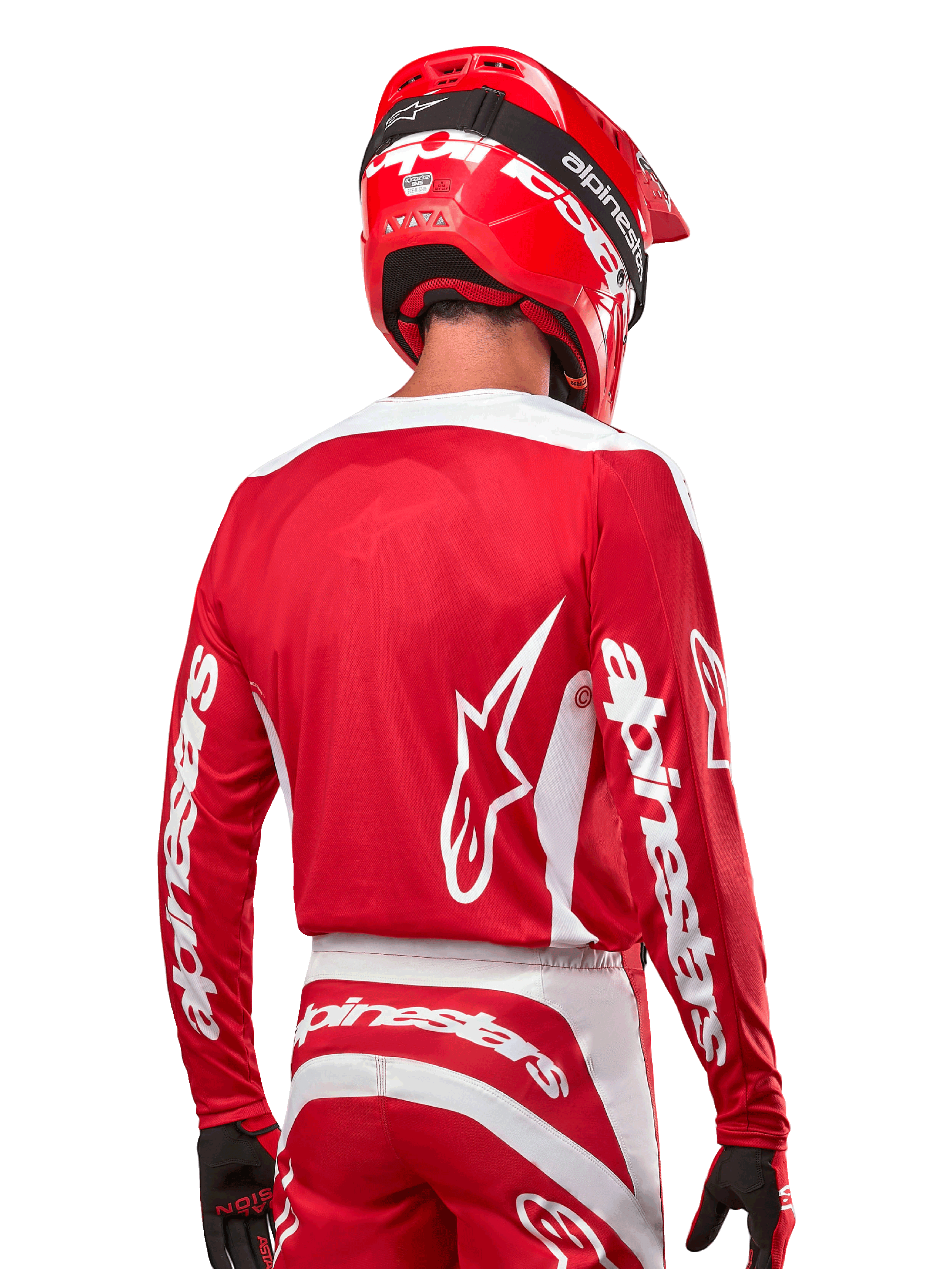 Kierowca motocrossowy w koszulce Alpinestars 2024 Fluid Lurv, kolor czerwono-biały, widok z tyłu ukazujący białe logo Alpinestars na plecach i branding na rękawach, w zestawie z dopasowanym czerwonym kaskiem i czarnymi rękawicami, profesjonalna odzież do wyścigów off-road