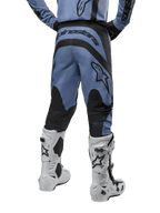 Alpinestars 2024 Fluid Lurv Pants, spodnie motocrossowe, jasnoniebieskie i czarne, widok z tyłu pokazujący czarne wzmocnione panele i duże logo marki, zestawione z biało-czarnymi butami motocrossowymi, profesjonalny sprzęt wyścigowy do jazdy terenowej