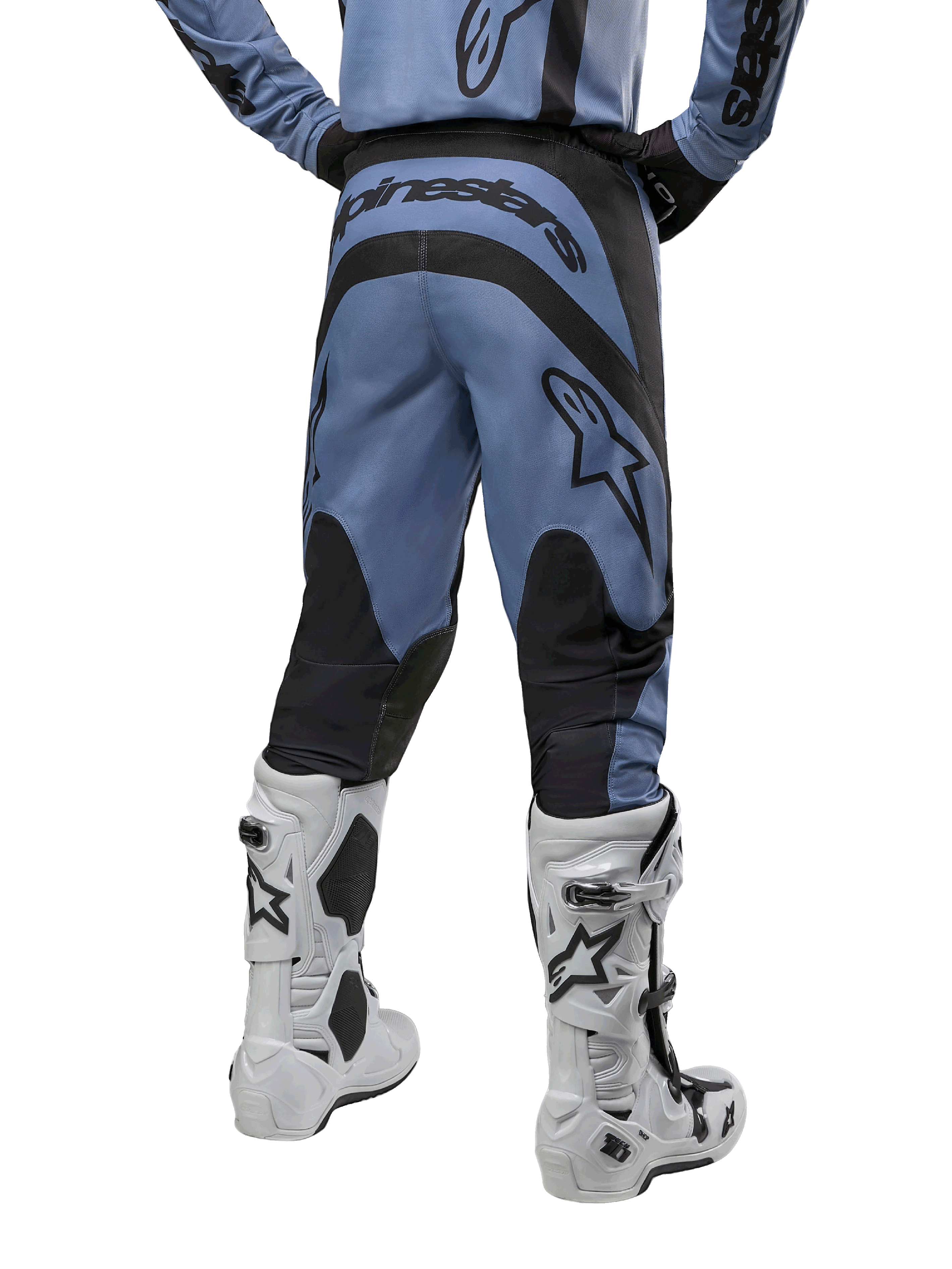 Alpinestars 2024 Fluid Lurv Pants, spodnie motocrossowe, jasnoniebieskie i czarne, widok z tyłu pokazujący czarne wzmocnione panele i duże logo marki, zestawione z biało-czarnymi butami motocrossowymi, profesjonalny sprzęt wyścigowy do jazdy terenowej