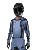 Motocyklista motocrossowy w koszulce Alpinestars 2024 Fluid Lurv, jasnoniebieska z czarnym, w zestawie z czarnym kaskiem i goglami, z wyraźnymi czarnymi akcentami graficznymi i logo gwiazdy Alpinestars, sportowa odzież wyczynowa do wyścigów terenowych