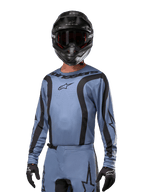 Motocyklista motocrossowy w koszulce Alpinestars 2024 Fluid Lurv, jasnoniebieska z czarnym, w zestawie z czarnym kaskiem i goglami, z wyraźnymi czarnymi akcentami graficznymi i logo gwiazdy Alpinestars, sportowa odzież wyczynowa do wyścigów terenowych
