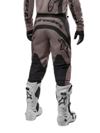Alpinestars 2024 Fluid Lurv Pants, spodnie motocrossowe, kolor Mud Black, widok z tyłu ukazujący duże czarne logo Alpinestars na siedzeniu oraz czarne panele na łydkach, zestawione z biało-czarnymi butami motocrossowymi i pasującą koszulką