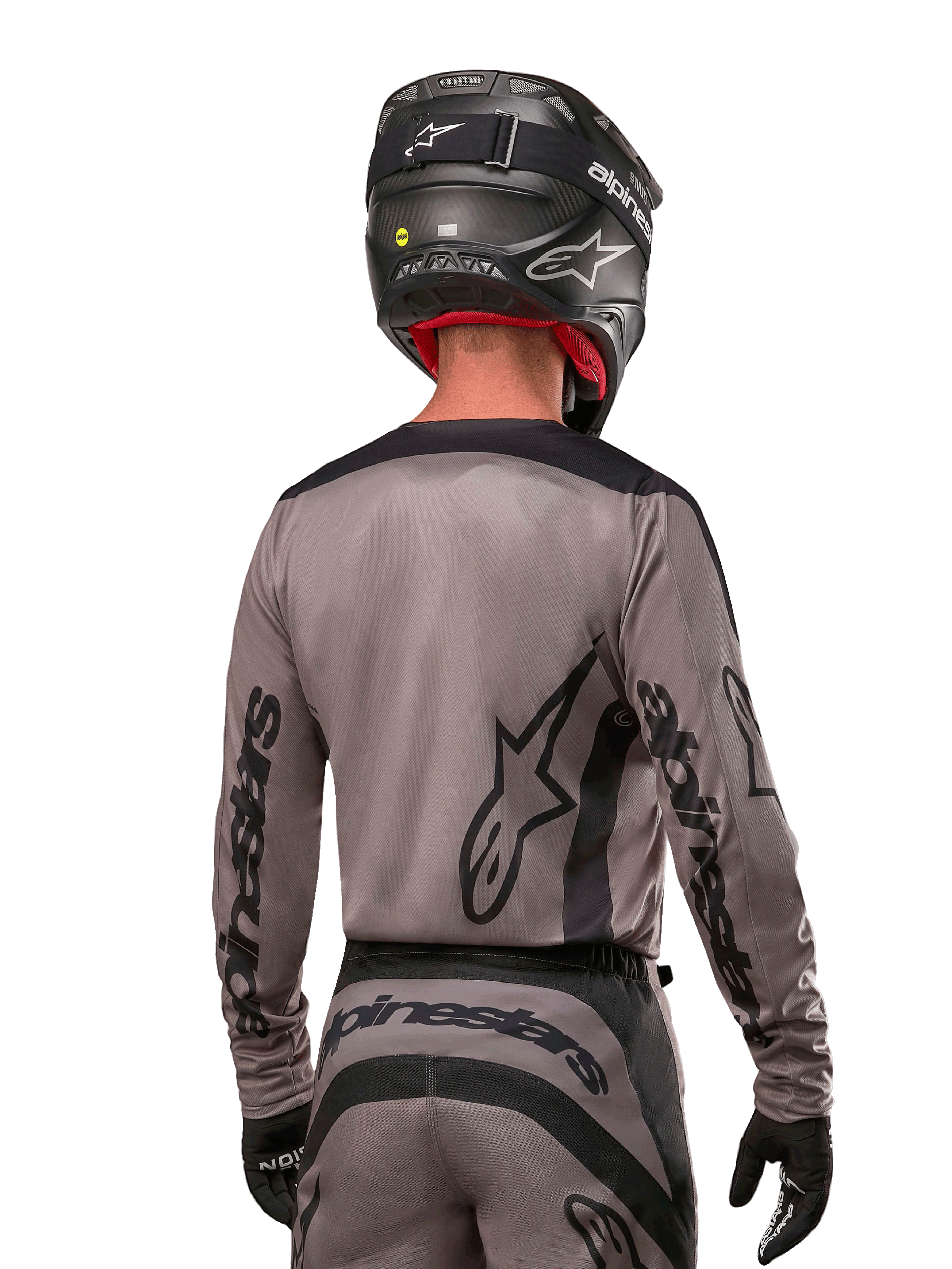Motocyklista motocrossowy widziany od tyłu w koszulce Alpinestars 2024 Fluid Lurv w kolorze Mud Black, czarne logo Alpinestars na rękawach i plecach, czarny kask i dopasowany sprzęt do wyścigów terenowych