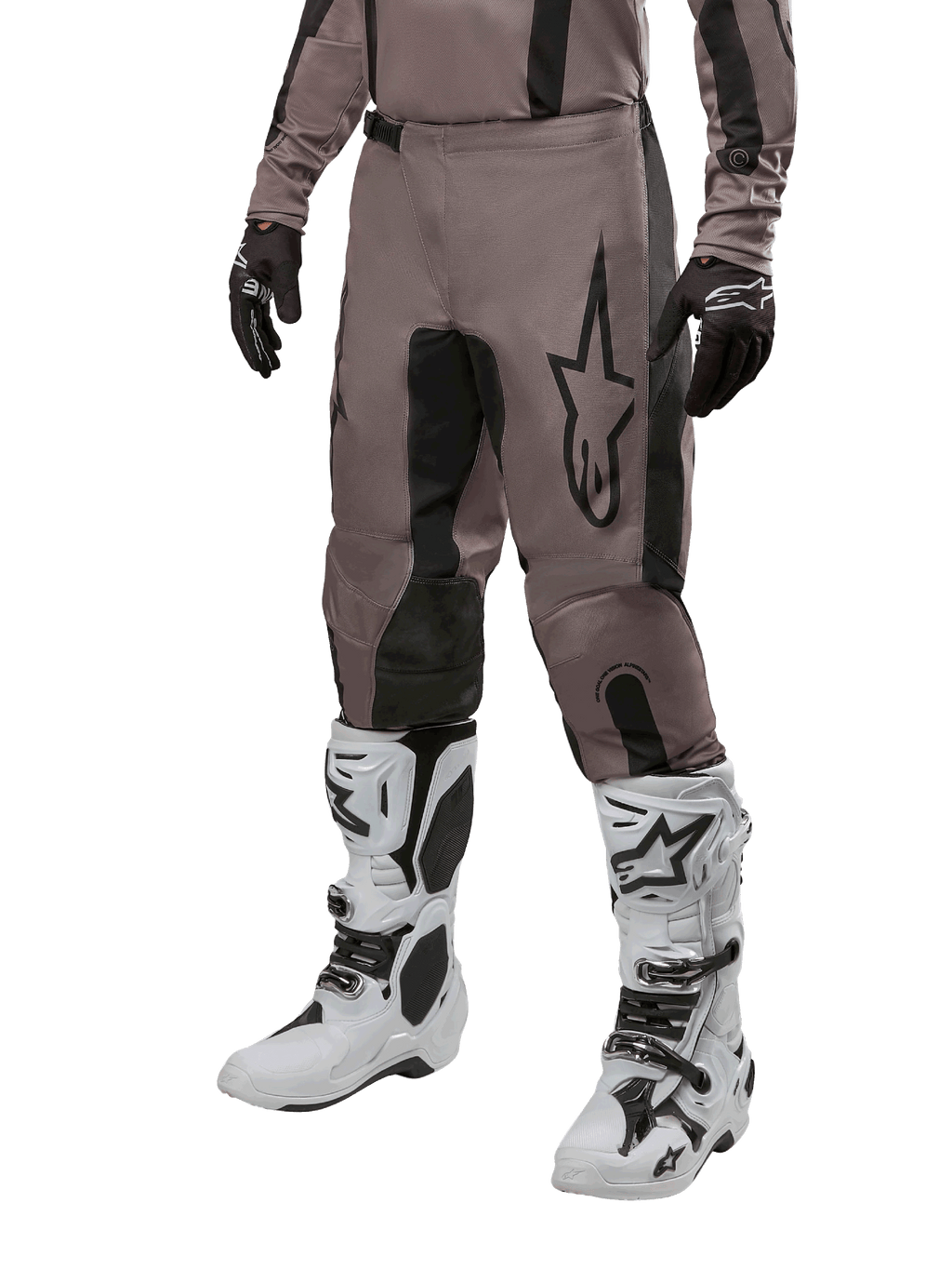 Alpinestars 2024 Fluid Lurv Pants, spodnie motocrossowe, kolor Mud Black i czarny, z logo Alpinestars, noszone z czarnymi rękawicami i białymi butami motocrossowymi, sportowy design do wyścigów terenowych