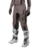 Alpinestars 2024 Fluid Lurv Pants, spodnie motocrossowe, kolor Mud Black i czarny, z logo Alpinestars, noszone z czarnymi rękawicami i białymi butami motocrossowymi, sportowy design do wyścigów terenowych