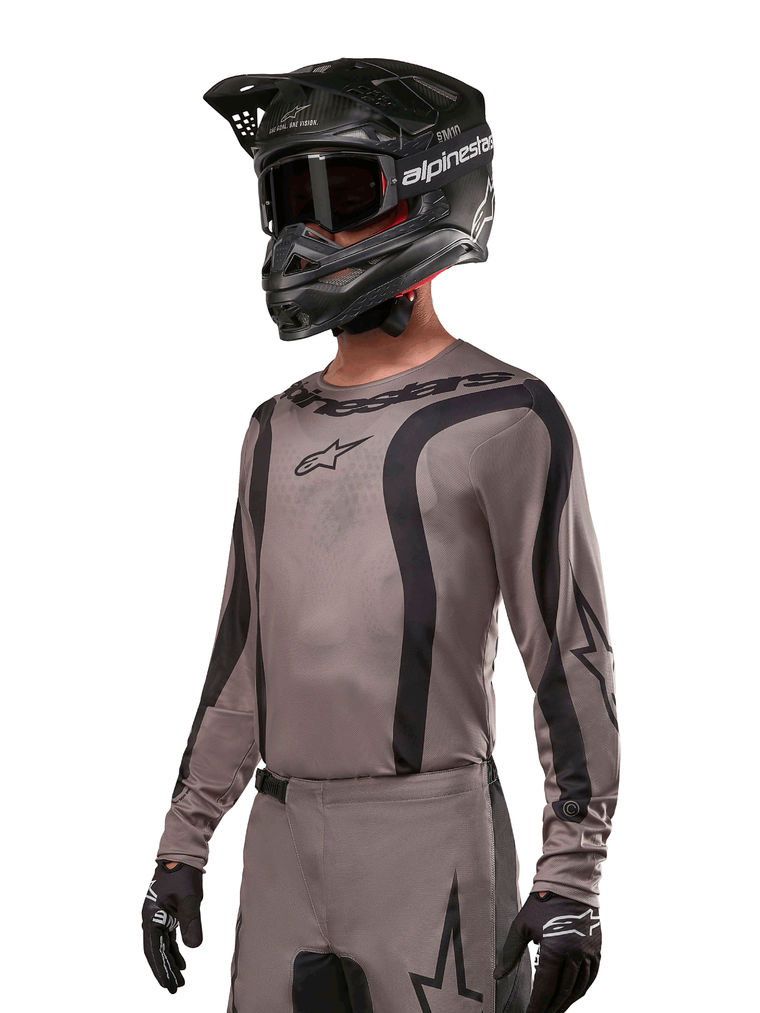 Alpinestars 2024 Fluid Lurv Jersey, koszulka motocrossowa w kolorze szarym i czarnym (Mud Black), model z długim rękawem, czarnymi zakrzywionymi pasami i logo, zestawiona z pasującymi spodniami i czarnym kaskiem motocrossowym, profesjonalny strój off-road