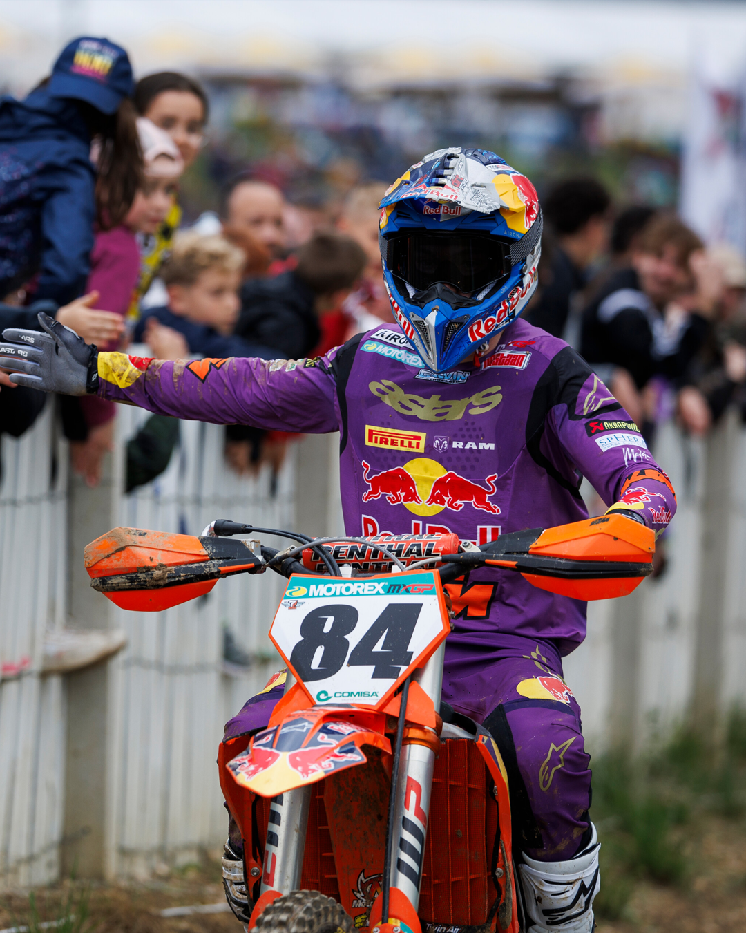 Motocross rider in purple Alpinestars gear with number 84 on a KTM bike, surrounded by spectators.