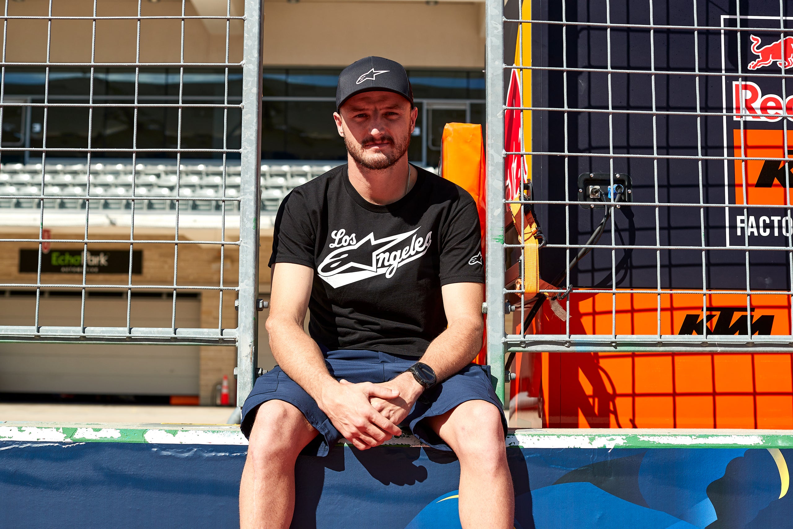 Jack Miller wearing Alpinestars clothing and sitting on a blue surface with a Red Bull branded background