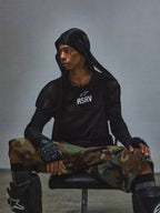 RSRV Nucleon SS Tee, Black T-shirt with white RSRV logo, worn with black hoodie, camouflage pants, fingerless gloves, and knee pads, urban tactical style, Alpinestars lifestyle collection