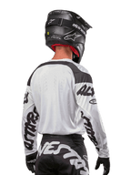 Koszulka Alpinestars Racer Hana 2024, biało-czarna, widok z tyłu prezentujący ergonomiczny krój i wyraźne logo na rękawach, zestawiona z czarnym kaskiem motocrossowym i pasującymi czarno-białymi spodniami, profesjonalny sprzęt wyścigowy do jazdy terenowej