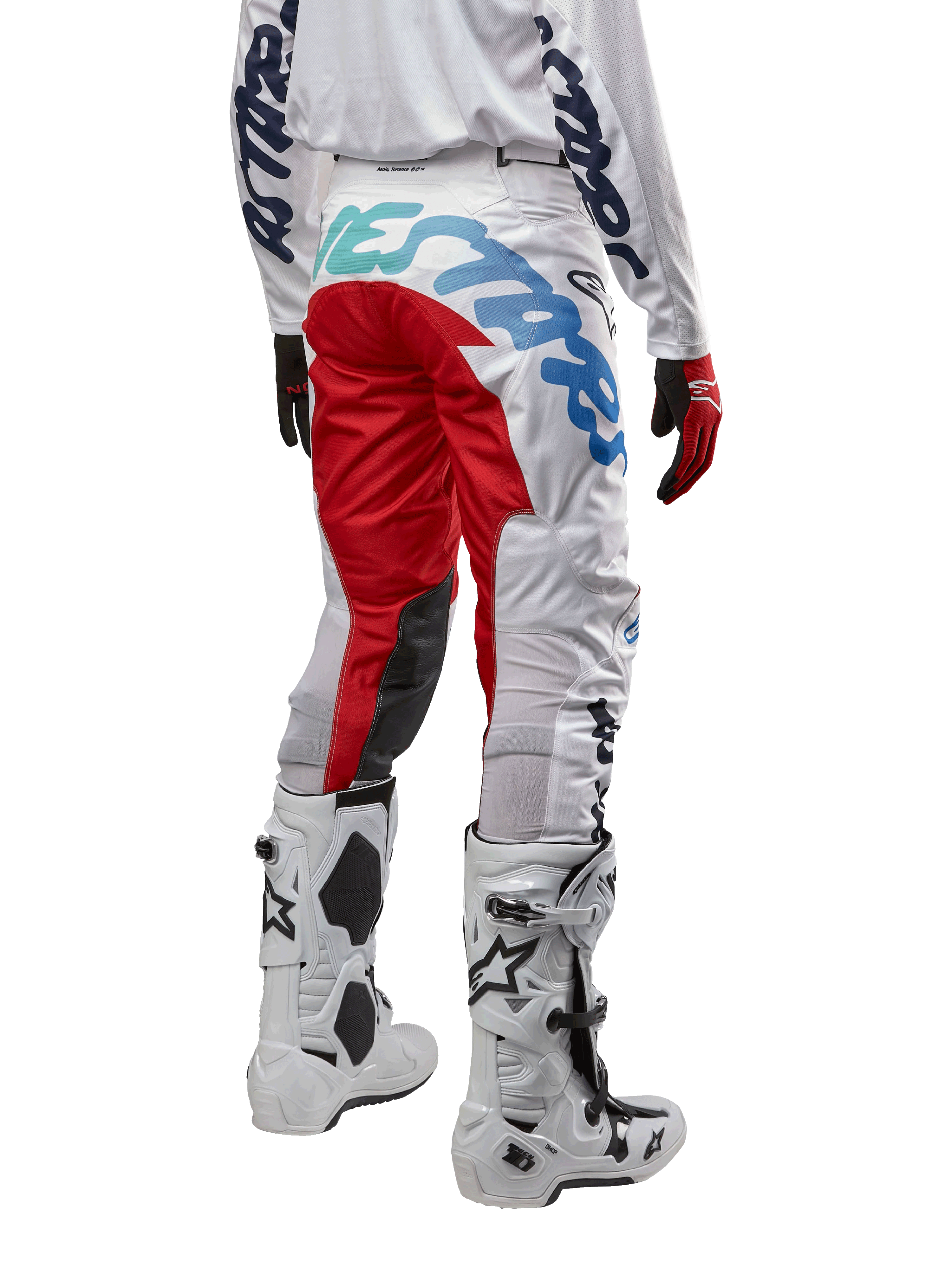 Alpinestars Racer Hana Pants 2024, spodnie motocrossowe, wielokolorowe białe z czerwonymi i niebieskimi akcentami, widok z tyłu pokazujący duże logo na siedzeniu, noszone z biało-czarnymi butami motocrossowymi, zaprojektowane dla wydajności i trwałości w terenie