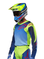 Koszulka Alpinestars Racer Hoen 2024, koszulka motocrossowa, kolory żółty fluo i granatowy z czerwonymi logotypami, noszona z pasującym żółto-niebiesko-czerwonym kaskiem i niebieskimi rękawicami, wyrazisty strój do jazdy terenowej