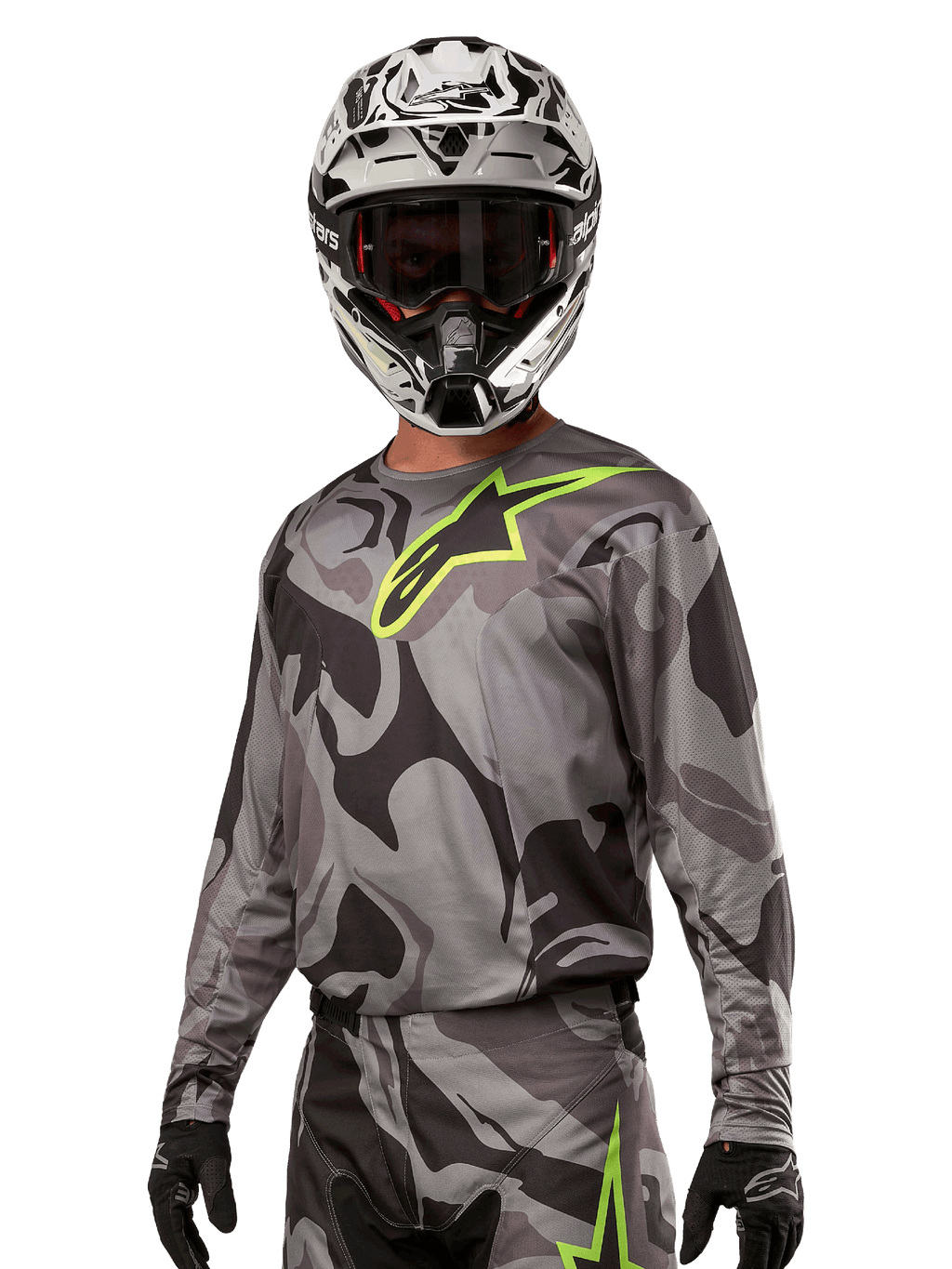 Alpinestars 2024 Racer Tactical Jersey, koszulka motocrossowa, szary kamuflaż Cast Gray Camo Magnet z neonowo zielonym logo, noszona z czarno-białym kaskiem i czarnymi rękawicami, techniczna tkanina odprowadzająca wilgoć do jazdy terenowej