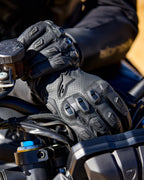 Alpinestars SP X 7 Gloves, czarne perforowane skórzane rękawice motocyklowe z ochraniaczami kostek TPU i ślizgaczami palców, widoczne na dłoniach motocyklisty trzymającego kierownicę motocykla