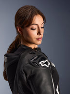 Kobieta w dwuczęściowym skórzanym kombinezonie Alpinestars Stella GP-R7, zbliżenie na ramię z czarnej skóry z ochraniaczem DFS RR i białym logo gwiazdy, zintegrowany garb aerodynamiczny i perforowane detale