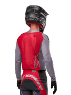 Kierowca motocrossowy widziany od tyłu w koszulce Alpinestars 2024 Supertech Dade w kolorze Iron Red Berry i szarym, z oddychającym panelem z siatki na plecach i srebrnymi akcentami logo, w zestawie z czarnym kaskiem i dopasowanymi spodniami wyścigowymi, zapewniający profesjonalną wydajność off-road