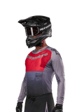 Alpinestars 2024 Supertech Dade Jersey, koszulka motocrossowa, czerwona (Iron Red Berry) i szara, długi rękaw z laserowymi perforacjami, zawodnik w czarnym kasku i rękawicach, profesjonalny sportowy krój wyścigowy