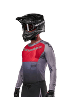 Alpinestars 2024 Supertech Dade Jersey, koszulka motocrossowa, czerwona (Iron Red Berry) i szara, długi rękaw z laserowymi perforacjami, zawodnik w czarnym kasku i rękawicach, profesjonalny sportowy krój wyścigowy