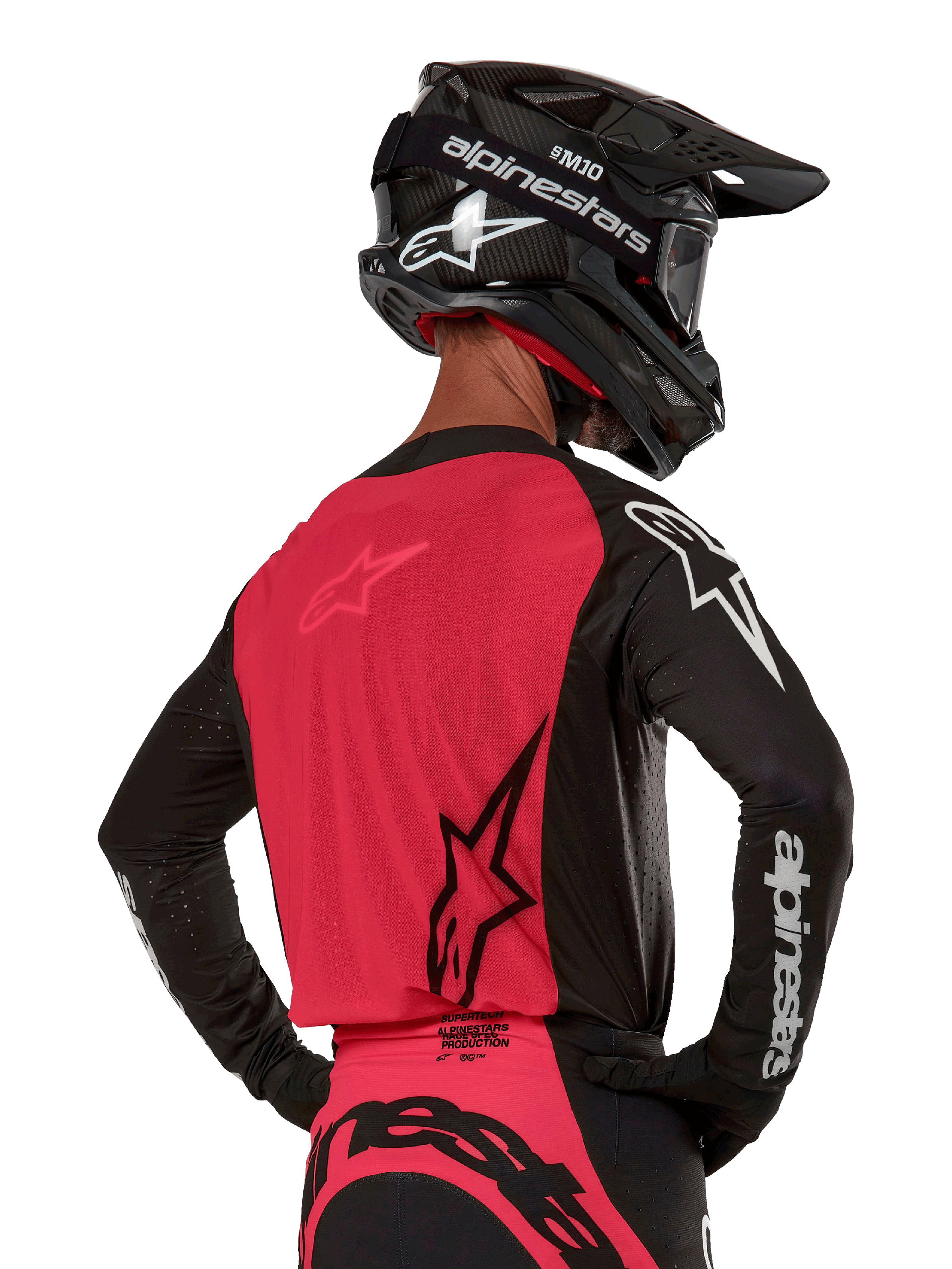 Alpinestars 2024 Supertech Ward Jersey, koszulka motocrossowa, czarno-czerwona (Red Berry), widok z tyłu prezentujący czerwony panel z siatki i czarne rękawy z białym brandingiem, zestawiona z czarnym kaskiem z włókna węglowego i rękawicami, sportowy krój wyścigowy do jazdy terenowej
