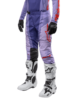 Alpinestars Techstar Ocuri Pants 2024, spodnie motocrossowe, fioletowe z jaskrawopomarańczowymi detalami, czerwone logo, białe buty motocrossowe i czarne rękawice, sportowy design off-road