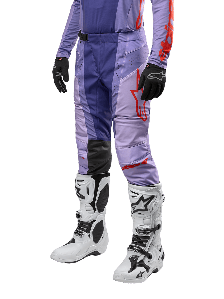 Alpinestars Techstar Ocuri Pants 2024, spodnie motocrossowe, fioletowe z jaskrawopomarańczowymi detalami, czerwone logo, białe buty motocrossowe i czarne rękawice, sportowy design off-road