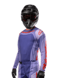 Alpinestars 2024 Techstar Ocuri Jersey, bluza motocrossowa, fioletowa i intensywnie pomarańczowa, długi rękaw z laserowo wycinanymi perforacjami dla wentylacji, atletyczny krój wyścigowy, noszona z czarnym kaskiem motocrossowym i rękawicami