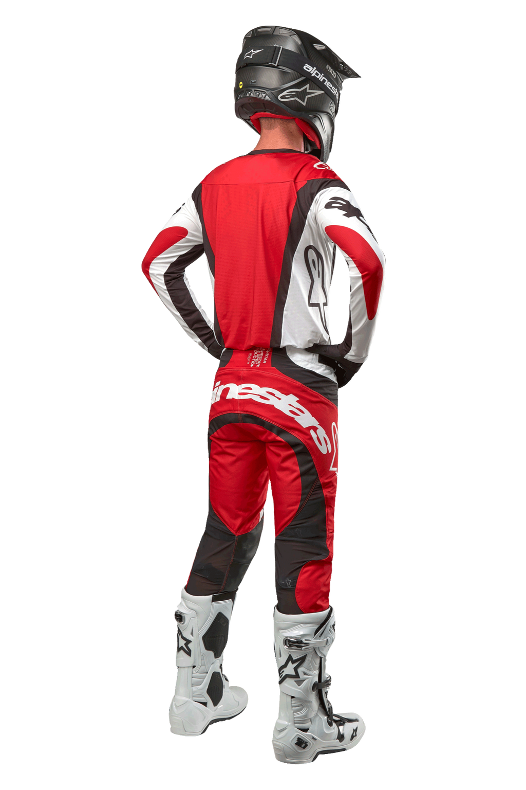 Alpinestars 2024 Techstar Ocuri Pants, spodnie motocrossowe, kolor Mars Red White Black, widok z tyłu na zawodnika motocrossowego w pełnym stroju wyścigowym, w tym pasującą bluzę, czarny kask oraz biało-czarne buty, podkreślający branding Alpinestars i trwałą konstrukcję materiału.