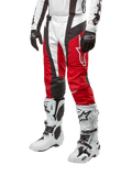 Spodnie Alpinestars 2024 Techstar Ocuri, spodnie motocrossowe, kolor czerwony Mars Red, biały i czarny, zestawione z dopasowaną biało-czarną koszulką, czarnymi rękawicami oraz białymi butami wyścigowymi z klamrami, techniczna odzież ochronna na białym tle.