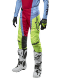 Alpinestars Techstar Ocuri Pants 2024, spodnie motocrossowe, jasnoniebieskie, czerwone i neonowo-żółte, noszone z dopasowaną odzieżą i białymi butami, z wyrazistym brandingiem Astars i wyczynowym krojem wyścigowym.