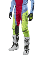 Alpinestars Techstar Ocuri Pants 2024, spodnie motocrossowe, jasnoniebieskie, czerwone i neonowo-żółte, noszone z dopasowaną odzieżą i białymi butami, z wyrazistym brandingiem Astars i wyczynowym krojem wyścigowym.