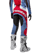 Spodnie Alpinestars Techstar Ocuri 2024, spodnie motocrossowe, jasnoniebieskie, czerwone i białe, widok z tyłu eksponujący duże czerwone logo Alpinestars na siedzeniu, zestawione z białymi butami wyścigowymi i dopasowaną bluzą.