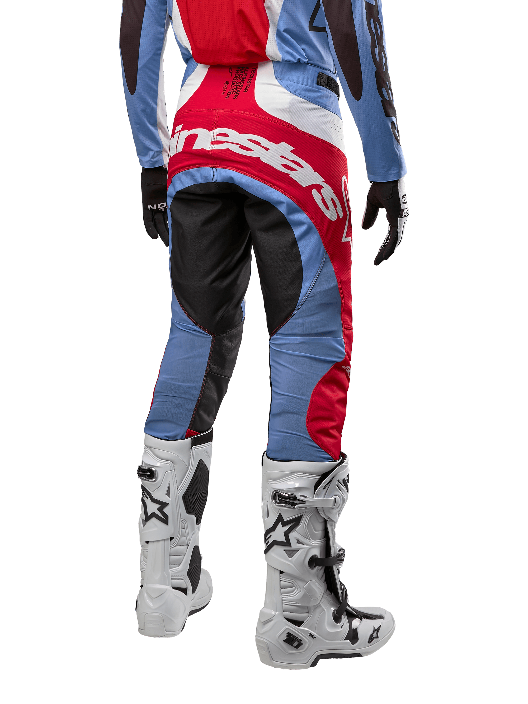 Spodnie Alpinestars Techstar Ocuri 2024, spodnie motocrossowe, jasnoniebieskie, czerwone i białe, widok z tyłu eksponujący duże czerwone logo Alpinestars na siedzeniu, zestawione z białymi butami wyścigowymi i dopasowaną bluzą.