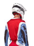 Alpinestars 2024 Techstar Ocuri Jersey, koszulka motocrossowa, jasnoniebieska, czerwona Mars Red i biała, widok z tyłu na motocyklistę w pasującym białym kasku i czarnych goglach, wyraźne czarne logo na rękawach, ergonomiczny krój wyścigowy dla wydajności off-road