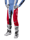Spodnie Alpinestars Techstar Ocuri 2024, spodnie motocrossowe, jasnoniebieskie, czerwone i białe, noszone z jasnoniebieską bluzą i białymi butami, z logo gwiazdy na udzie i wzmocnionymi kolanami, kompletny strój do wyścigów off-road