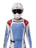 Koszulka Alpinestars 2024 Techstar Ocuri, koszulka do wyścigów motocrossowych, jasnoniebieska, czerwona i biała, widok z przodu z wentylacją wycinaną laserowo i sportowym krojem, noszona z białym kaskiem i goglami, profesjonalny styl off-road