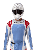 Koszulka Alpinestars 2024 Techstar Ocuri, koszulka do wyścigów motocrossowych, jasnoniebieska, czerwona i biała, widok z przodu z wentylacją wycinaną laserowo i sportowym krojem, noszona z białym kaskiem i goglami, profesjonalny styl off-road