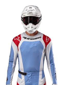Koszulka Alpinestars 2024 Techstar Ocuri, koszulka do wyścigów motocrossowych, jasnoniebieska, czerwona i biała, widok z przodu z wentylacją wycinaną laserowo i sportowym krojem, noszona z białym kaskiem i goglami, profesjonalny styl off-road