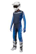 Alpinestars 2024 Techstar Pneuma Pants, spodnie motocrossowe, ciemnogranatowe i jasnoniebieskie, pełny zestaw wyścigowy z dopasowaną koszulką, biały kask z goglami, niebiesko-białe rękawice i białe buty, profesjonalny zestaw odzieży terenowej