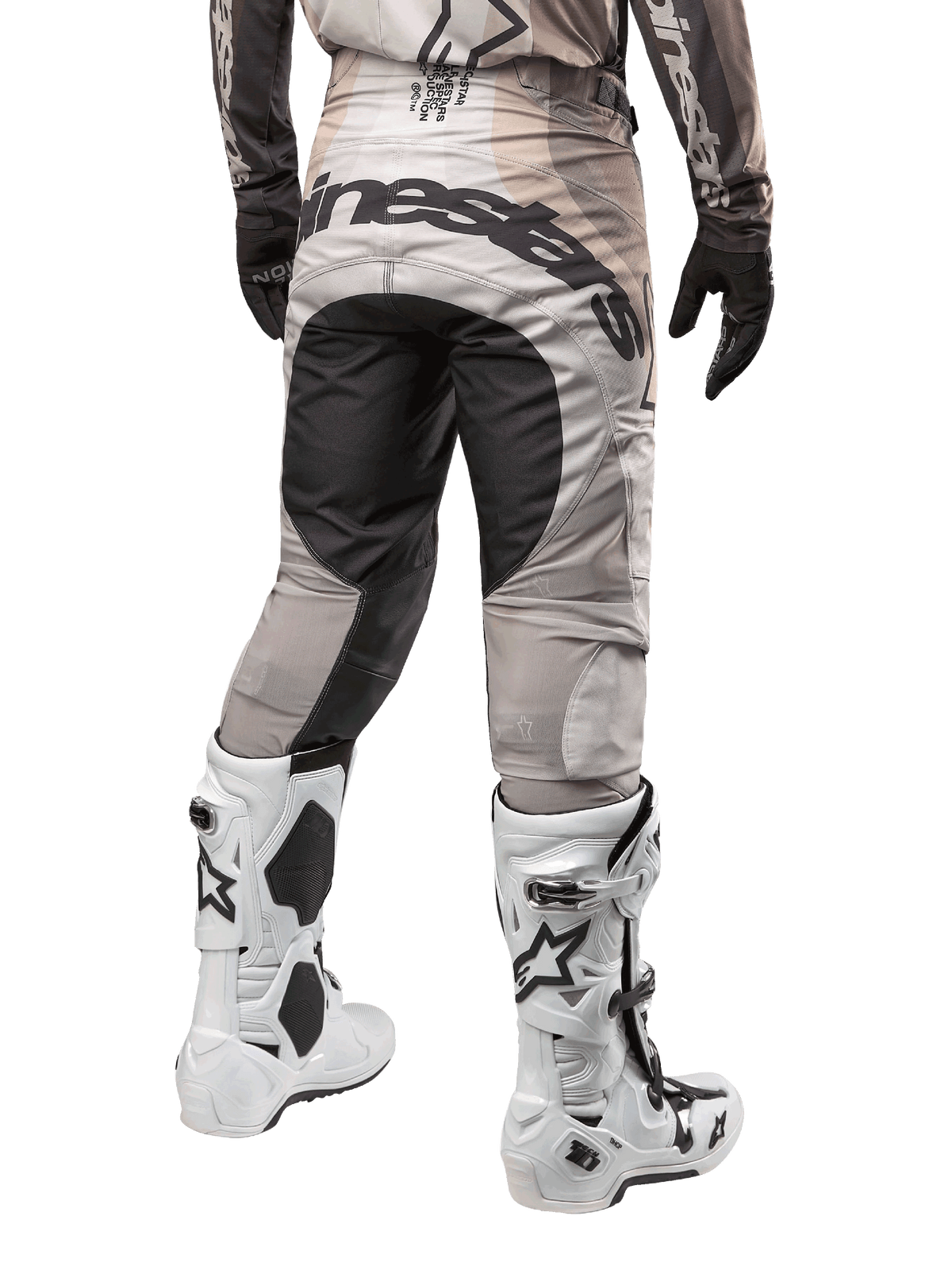 Alpinestars Techstar Pneuma 2024, spodnie motocrossowe, kolory Dark Sand i Iron Dust Gray, widok z tyłu od pasa w dół, wyraźne czarne logo Alpinestars na siedzeniu, noszone z biało-czarnymi butami motocrossowymi i czarnymi rękawicami, wytrzymała konstrukcja o wyścigowym kroju