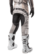 Alpinestars Techstar Pneuma 2024, spodnie motocrossowe, kolory Dark Sand i Iron Dust Gray, widok z tyłu od pasa w dół, wyraźne czarne logo Alpinestars na siedzeniu, noszone z biało-czarnymi butami motocrossowymi i czarnymi rękawicami, wytrzymała konstrukcja o wyścigowym kroju