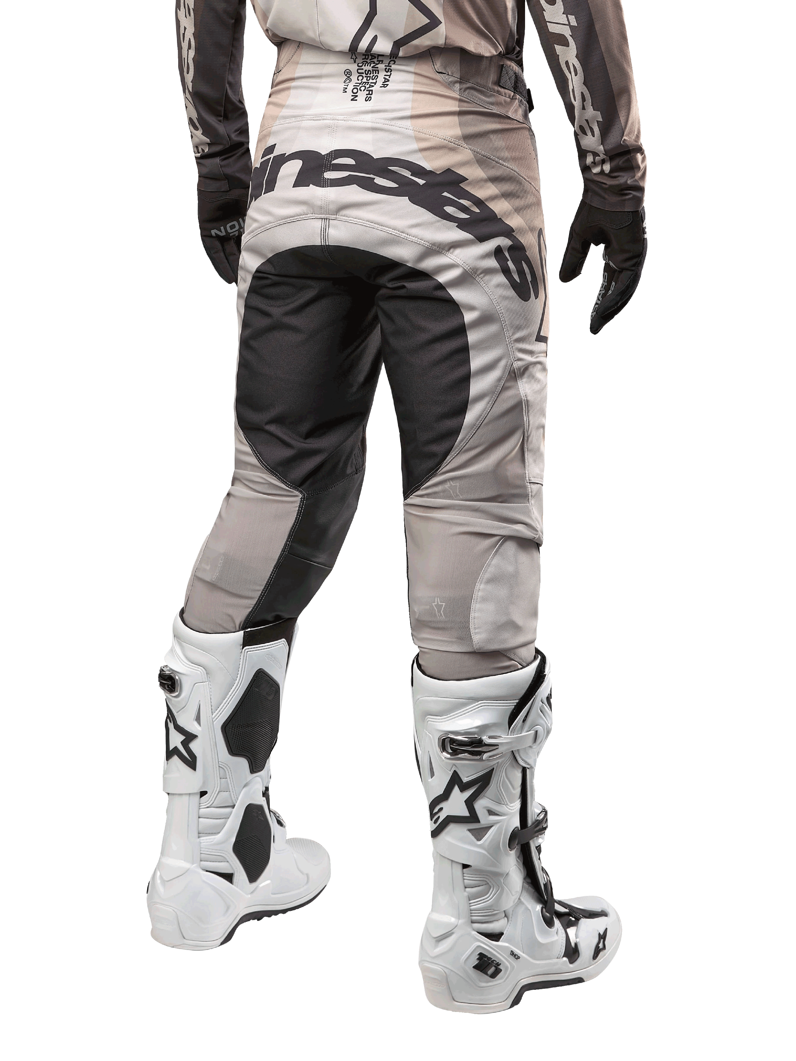 Alpinestars Techstar Pneuma 2024, spodnie motocrossowe, kolory Dark Sand i Iron Dust Gray, widok z tyłu od pasa w dół, wyraźne czarne logo Alpinestars na siedzeniu, noszone z biało-czarnymi butami motocrossowymi i czarnymi rękawicami, wytrzymała konstrukcja o wyścigowym kroju