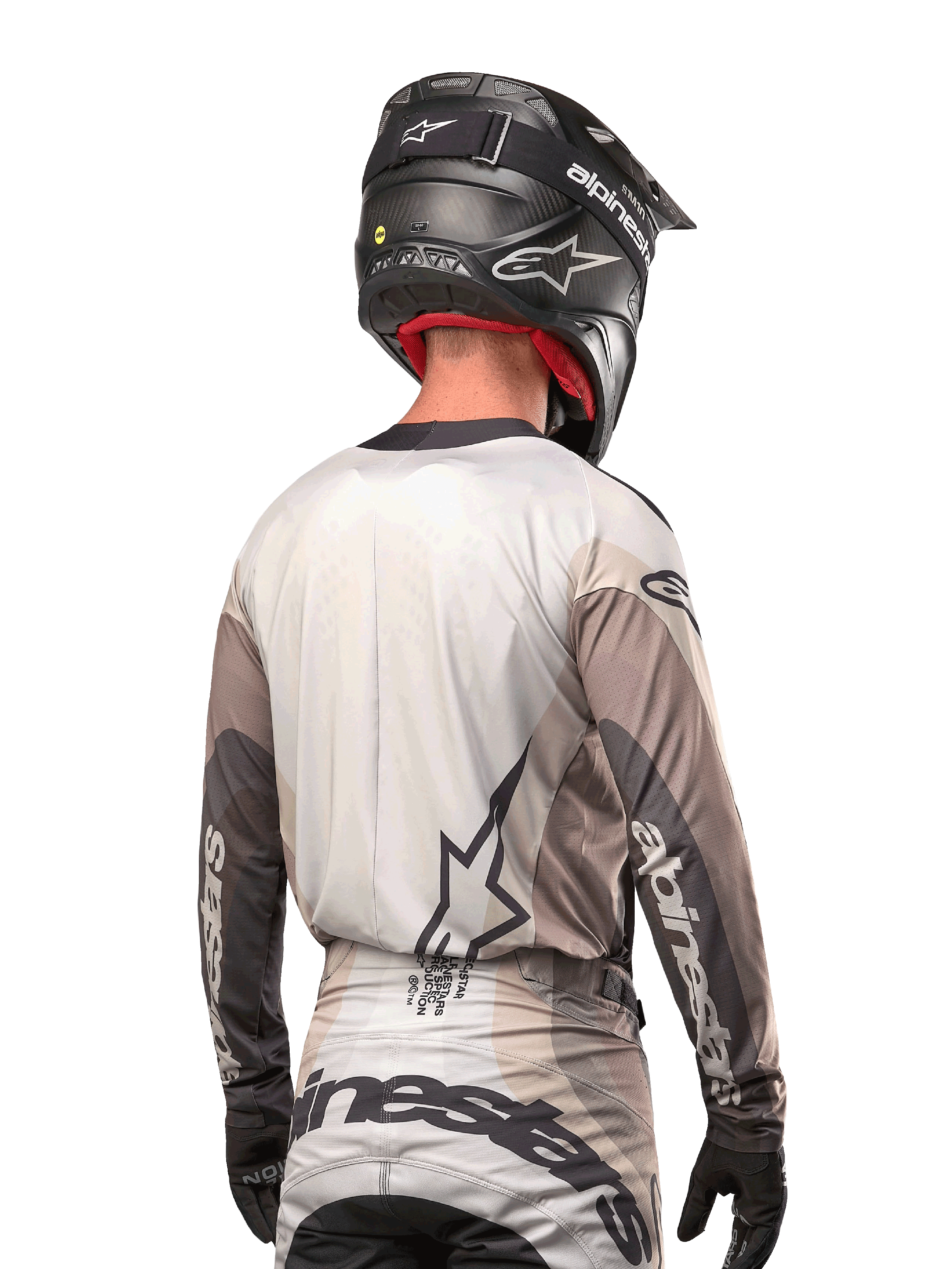 Kierowca motocrossowy widoczny od tyłu, koszulka Alpinestars 2024 Techstar Pneuma w kolorze Dark Sand Iron Dust Gray, czarny kask o karbonowym wykończeniu, duże logo gwiazdy na plecach i branding Alpinestars na rękawach.