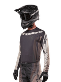 Alpinestars Techstar Pneuma Jersey 2024, koszulka motocrossowa, ciemnopiaskowa i szara (Iron Dust Gray), techniczna koszulka z długim rękawem, laserowo wycinane perforacje i białe logo, noszona z pasującymi spodniami i czarnym kaskiem, sportowy krój off-road
