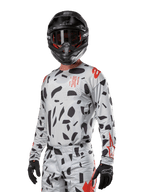 Alpinestars 2024 Techstar Rantera Jersey, koszulka motocrossowa, kolor Haze Gray Camo z czarnymi abstrakcyjnymi wzorami i czerwonymi akcentami, model z długim rękawem noszony z pasującym czarnym kaskiem i rękawicami, techniczna odzież do wyścigów terenowych