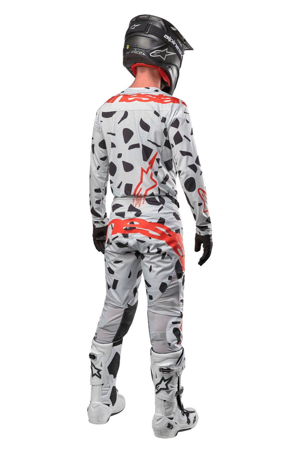 Motocyklista motocrossowy widoczny od tyłu, ubrany w spodnie Alpinestars 2024 Techstar Rantera, kolor Haze Gray Camo z czarnymi plamami i czerwonymi logotypami, pasująca koszulka, czarny kask i białe buty, kompletny strój wyścigowy off-road