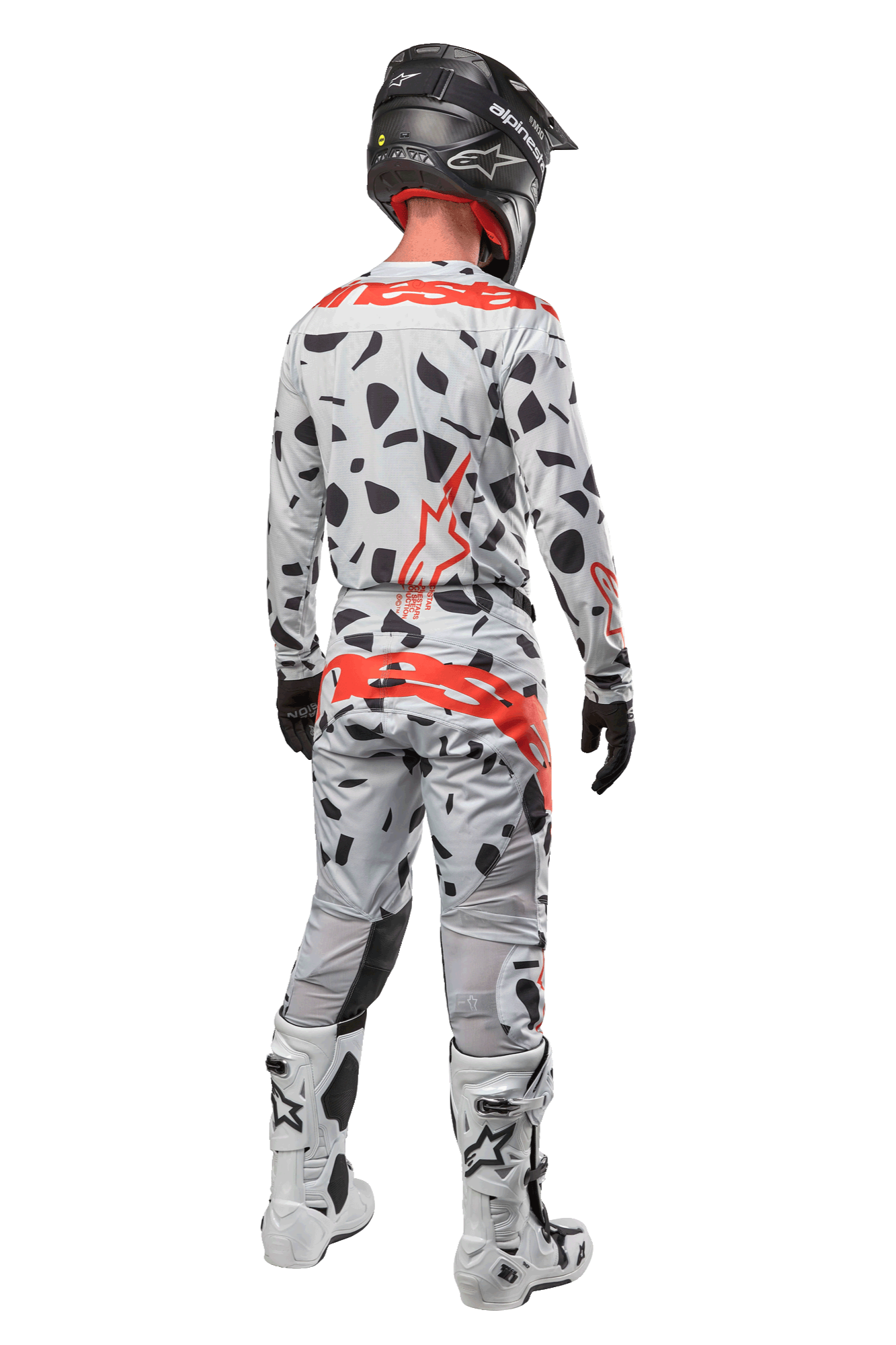 Motocyklista motocrossowy widoczny od tyłu, ubrany w spodnie Alpinestars 2024 Techstar Rantera, kolor Haze Gray Camo z czarnymi plamami i czerwonymi logotypami, pasująca koszulka, czarny kask i białe buty, kompletny strój wyścigowy off-road