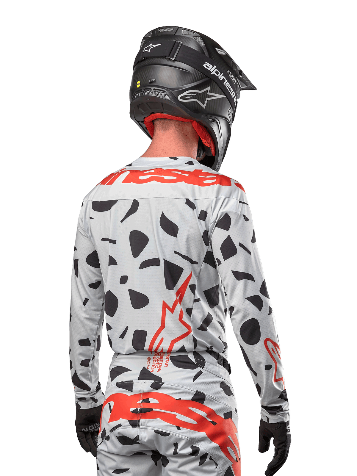 Motocyklista motocrossowy widziany od tyłu w koszulce Alpinestars 2024 Techstar Rantera w kolorze Haze Gray Camo, charakteryzującej się jasnoszarą bazą z czarnymi graficznymi wzorami oraz wyrazistym czerwonym logo Alpinestars na plecach i ramionach, w zestawie z pasującymi spodniami i czarnym kaskiem.