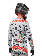 Motocyklista motocrossowy widziany od tyłu w koszulce Alpinestars 2024 Techstar Rantera w kolorze Haze Gray Camo, charakteryzującej się jasnoszarą bazą z czarnymi graficznymi wzorami oraz wyrazistym czerwonym logo Alpinestars na plecach i ramionach, w zestawie z pasującymi spodniami i czarnym kaskiem.